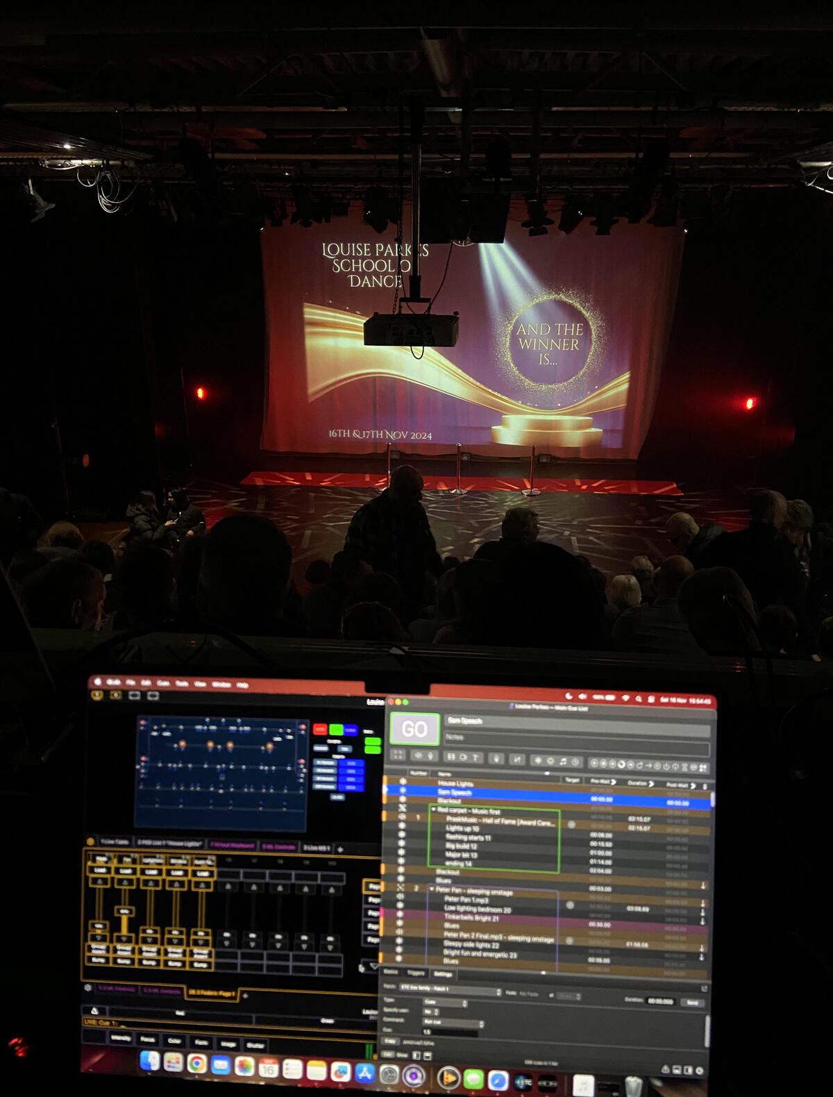 Computer screens displaying programs to control the stage lighting and other assets with the stage being visible in the distance.